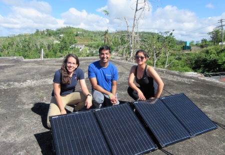 Ahumada, Keerthisinghe, and Kang with recently-installed solar cells on the roof of the community center.