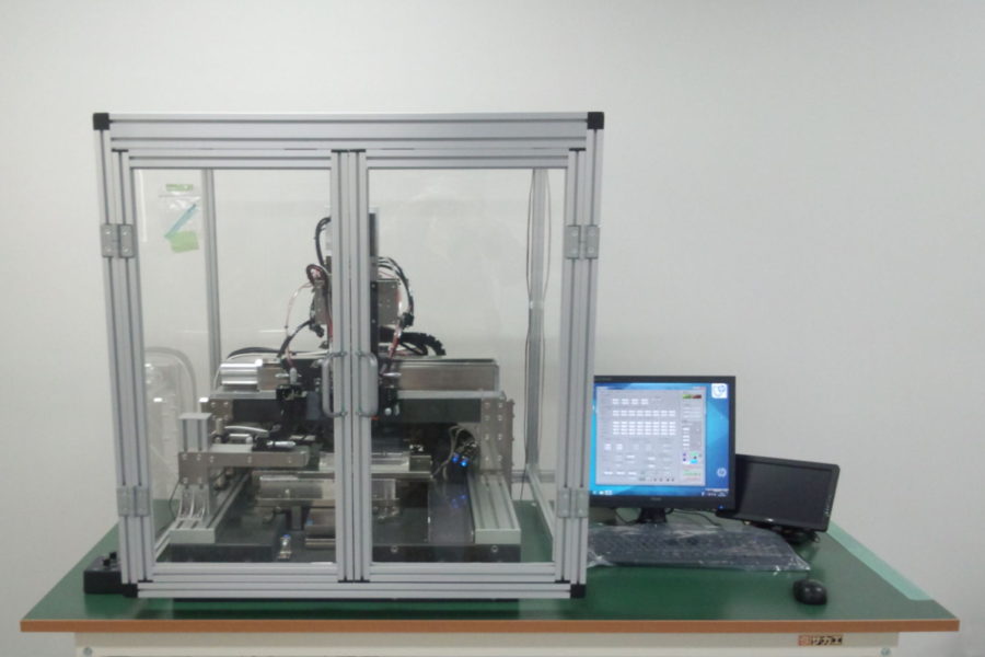 Printing machinery enclosed in a glass box next to a desktop computer.