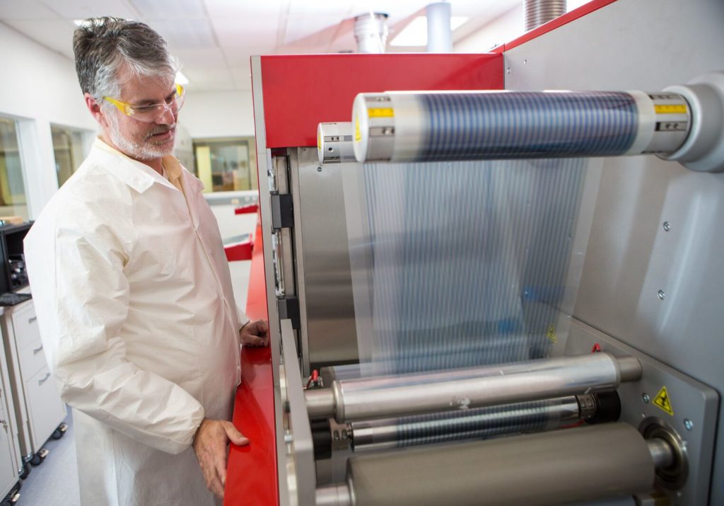 Washington Clean Energy Testbeds Technical Director J. Devin MacKenzie demonstrating the Testbeds' multi-stage roll-to-roll printer for flexible electronics.