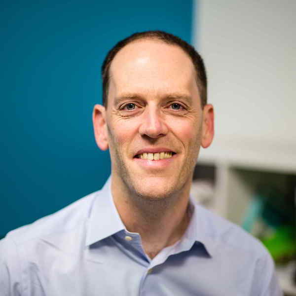 A middle-aged man in a collared shirt smiles for the camera.