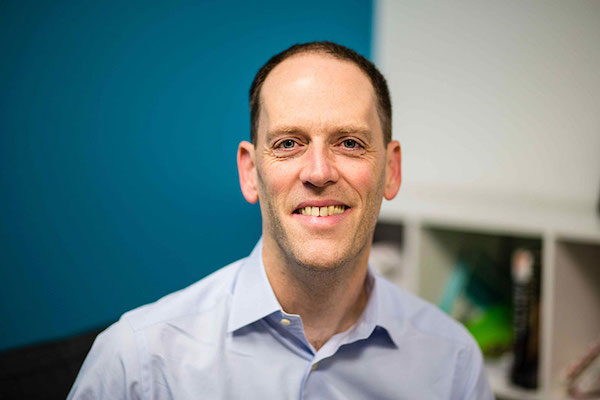 A man in a collared shirt smiles for the camera.