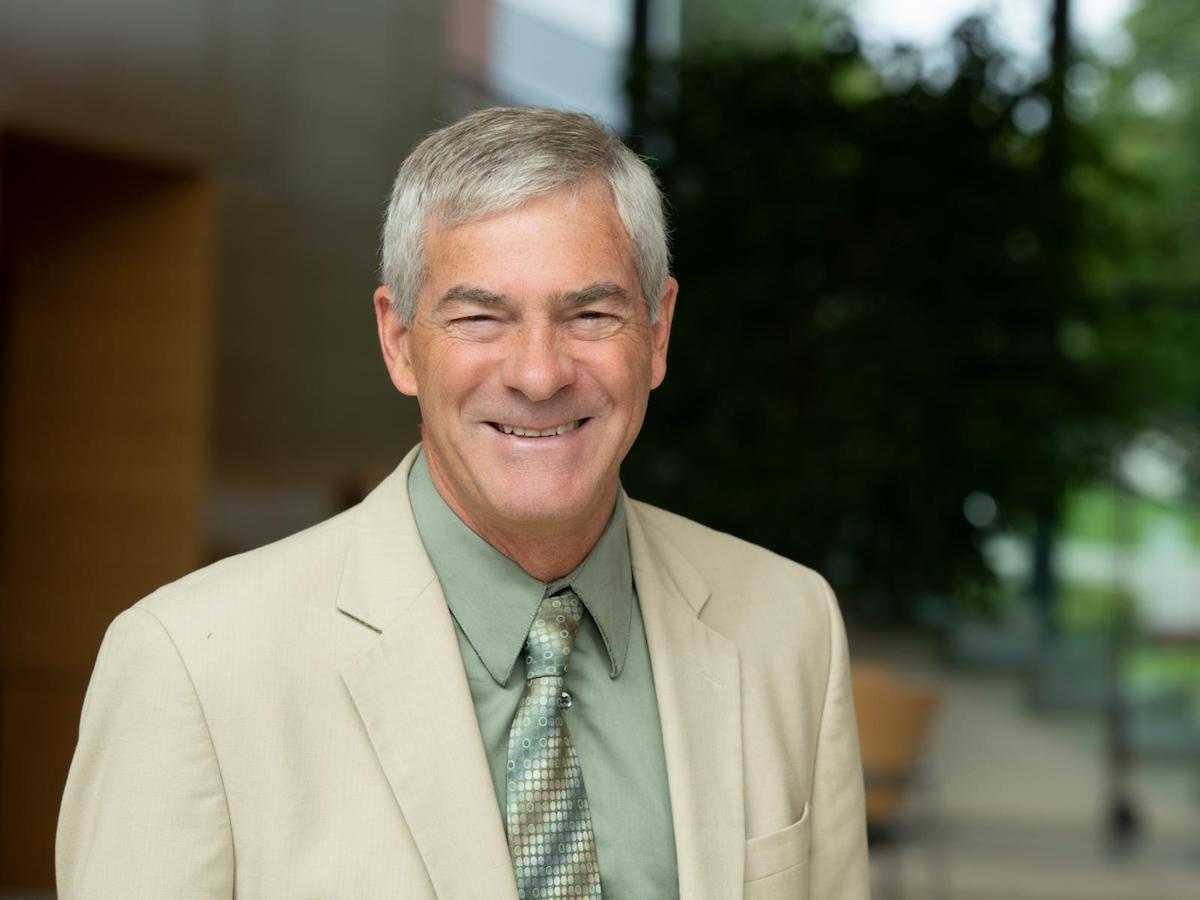 Jim De Yoreo smiles for the camera wearing a tan suit, sage green shirt, and patterned green tie.