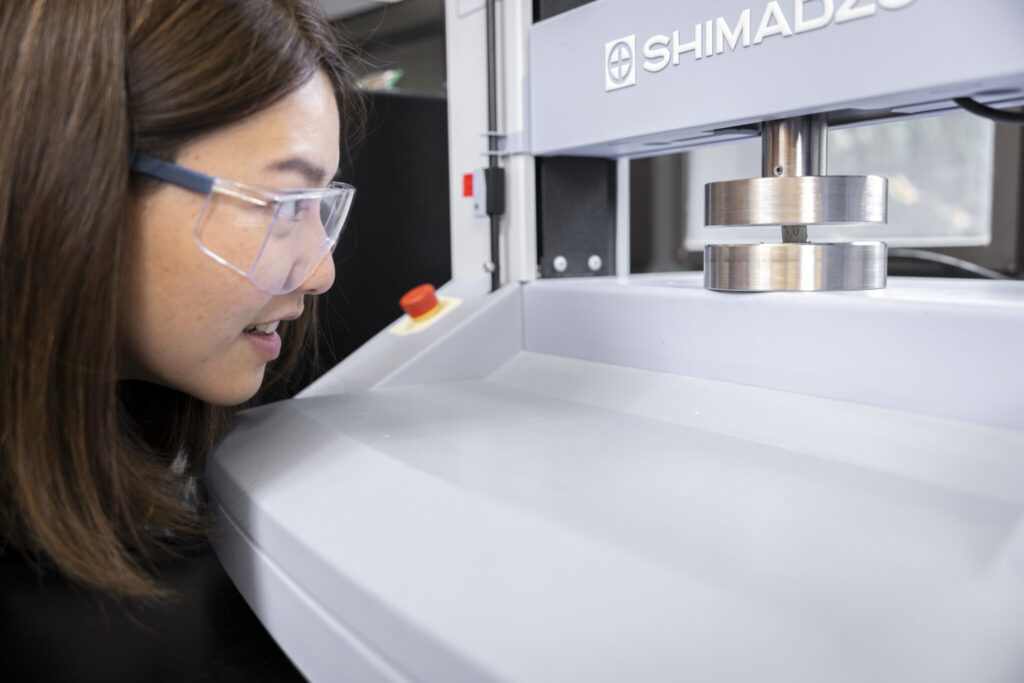 Researcher examining a piece of laboratory equipment that is stress testing the cement material